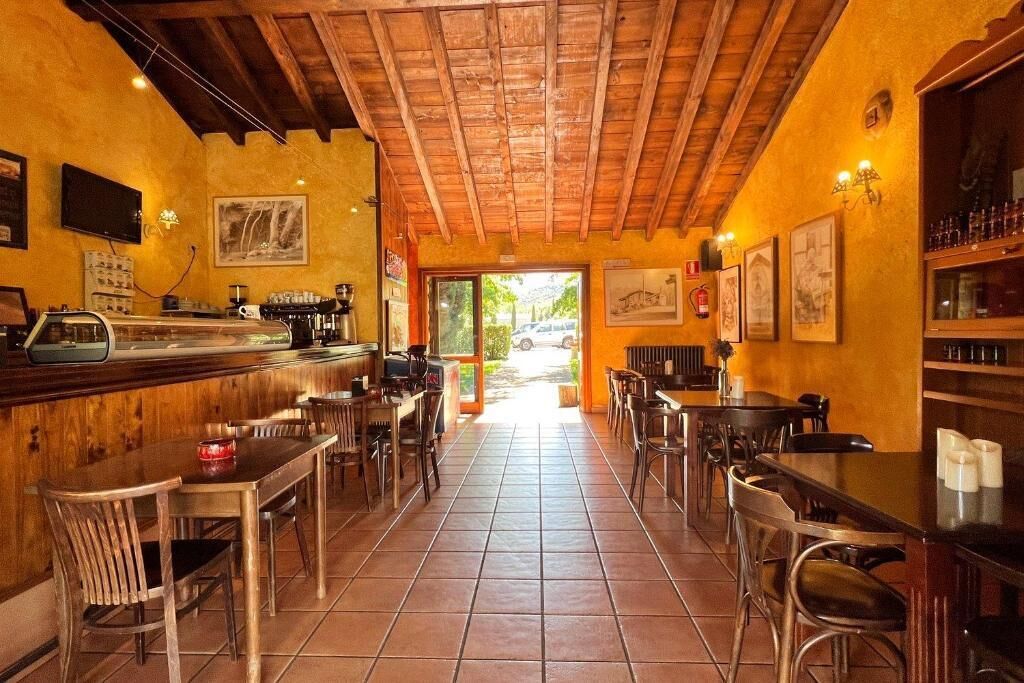 A restaurant interior with wooden ceiling beams, tiled floor, and bar area with stools and tables.