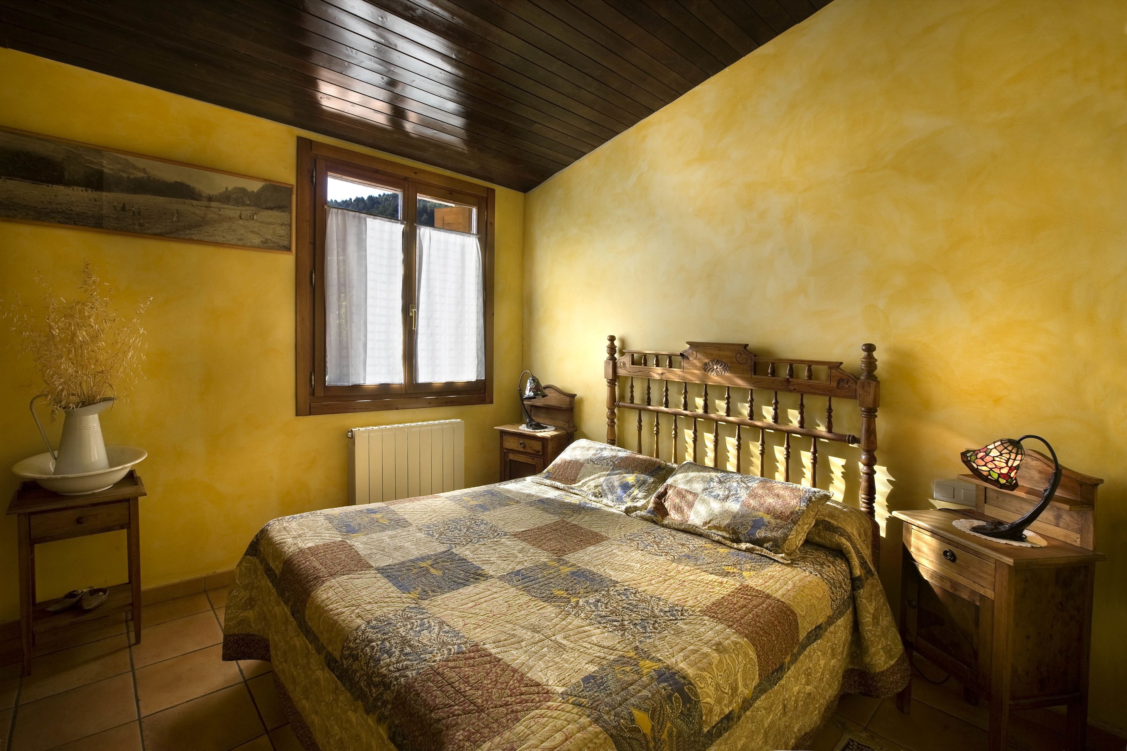 Une chambre à coucher avec un lit en bois, une table de chevet, une commode, une fenêtre avec des rideaux et un radiateur.