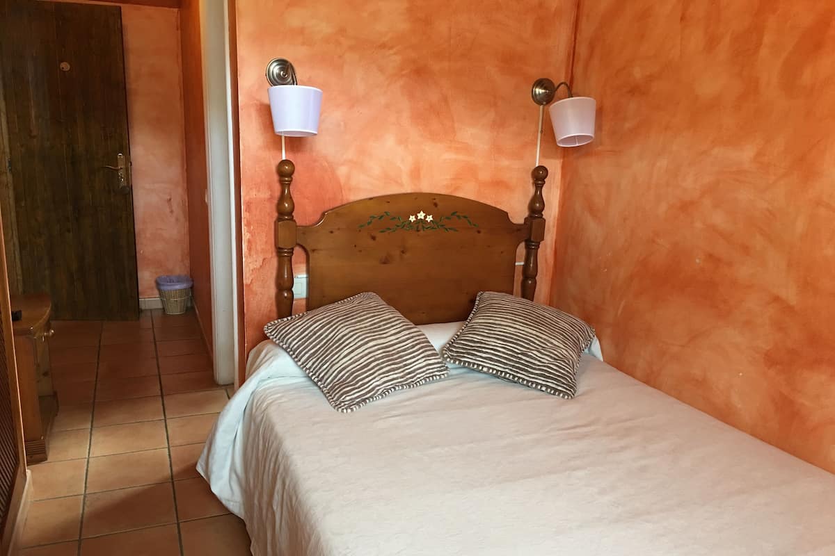 A bedroom with a wooden headboard, two wall-mounted lamps, a bed with striped pillows, and a tiled floor.