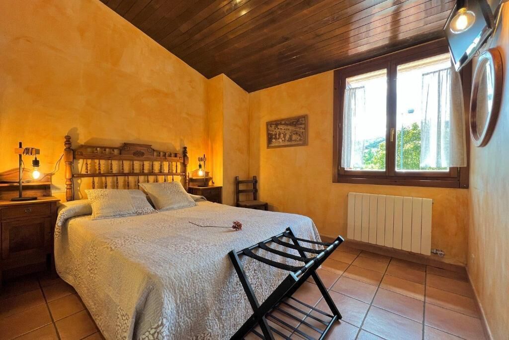 A bedroom with a large bed, wooden headboard, bedside tables, a radiator, and a window with curtains.