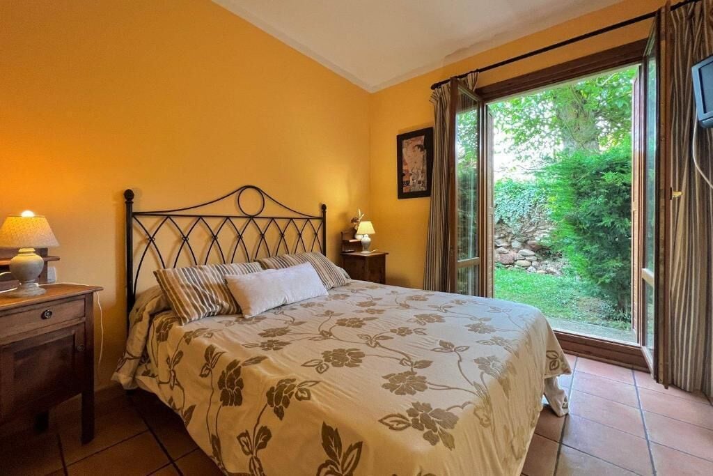Une chambre à coucher avec un lit, une table de chevet, une lampe et une fenêtre avec des rideaux.