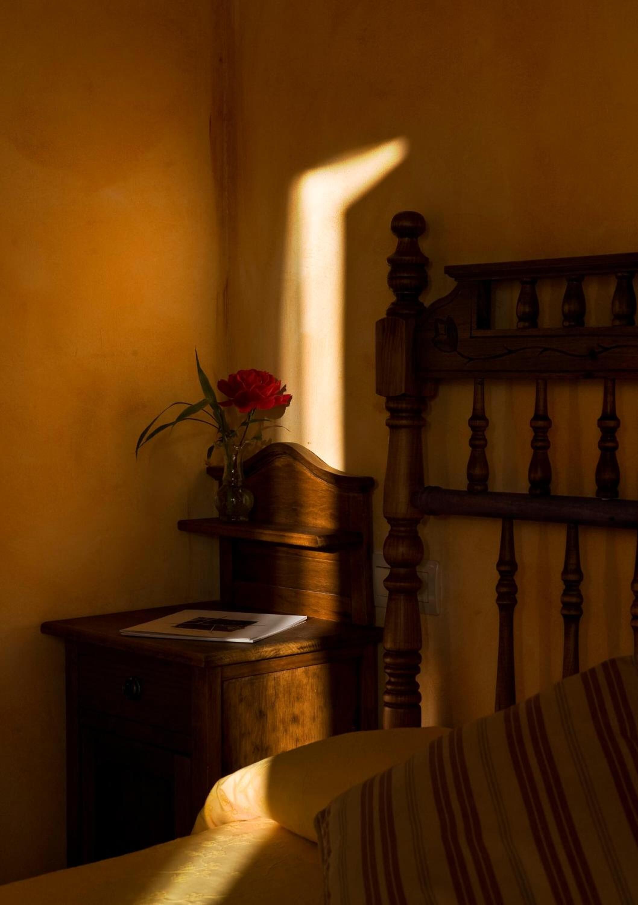 Quarto com cabeceira de madeira, mesa de cabeceira com um vaso de flores e cama com roupa de cama listrada.