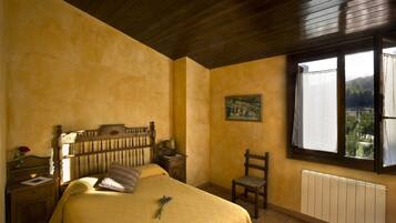 A bedroom with a wooden bed, a nightstand, a chair, a window with a view, and a radiator.