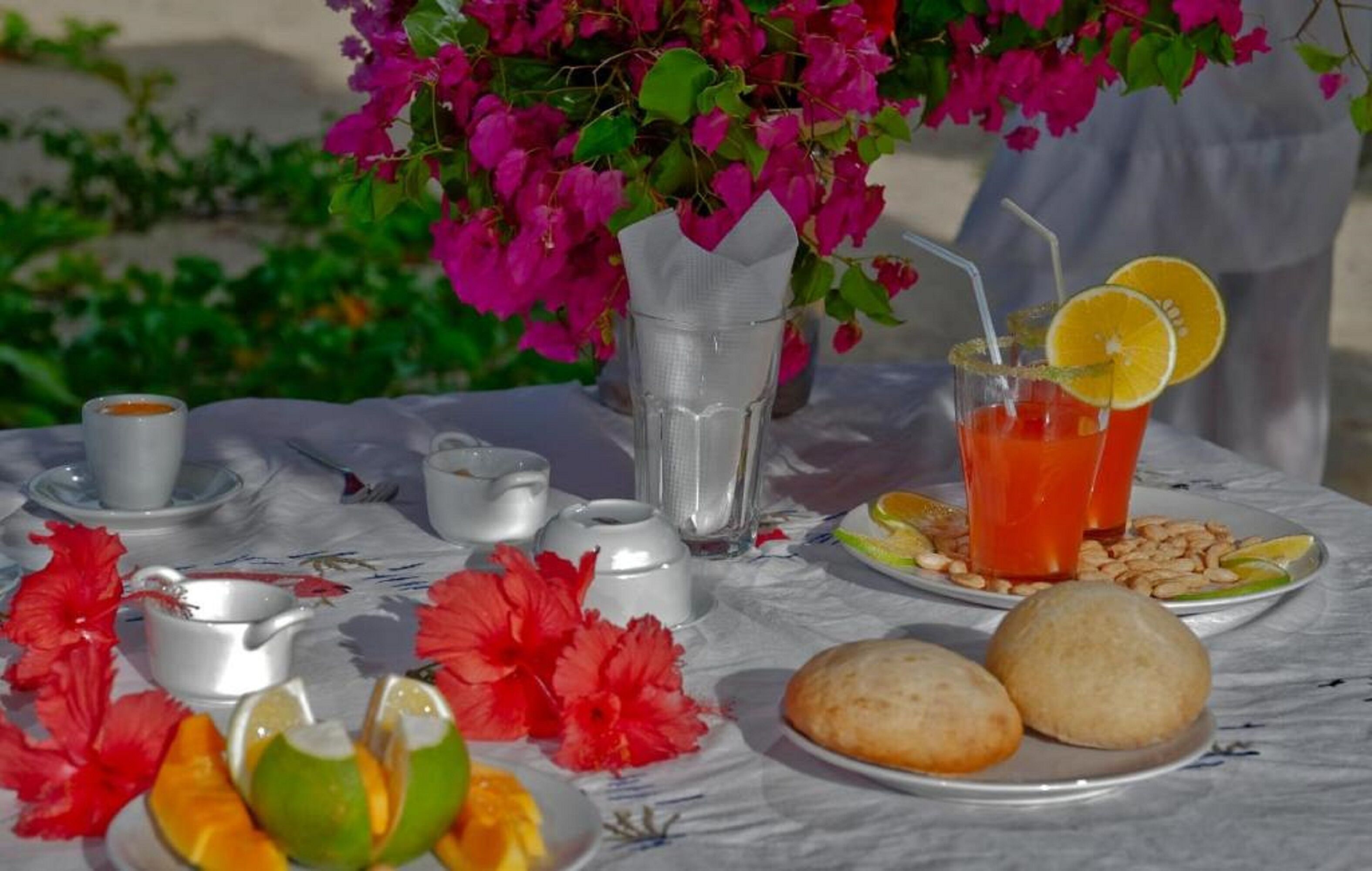 A table set with a drink, snacks, and a pitcher, surrounded by vibrant flowers.