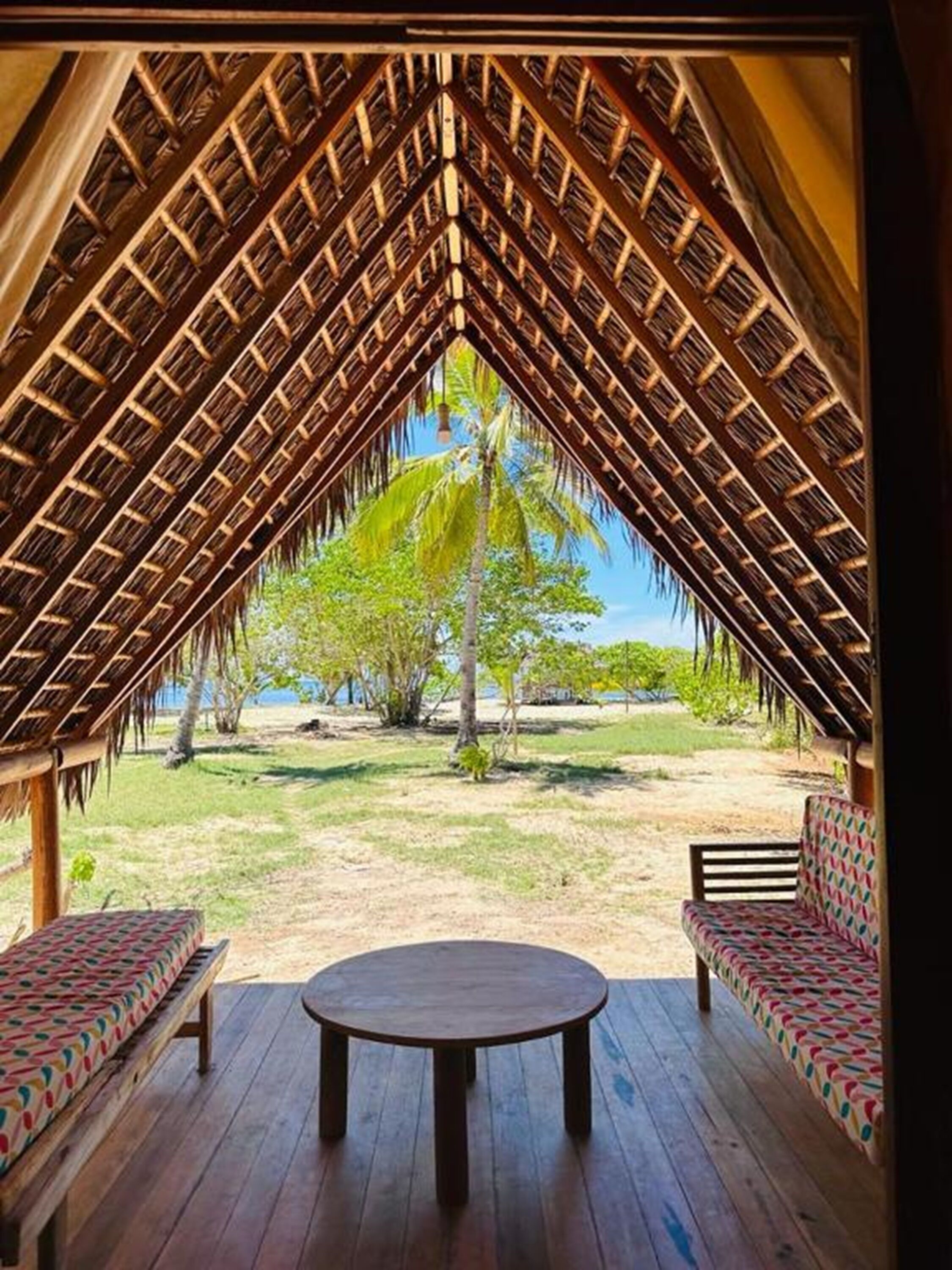 Una estructura al aire libre con techo de paja, una mesa redonda y dos sofás estampados.
