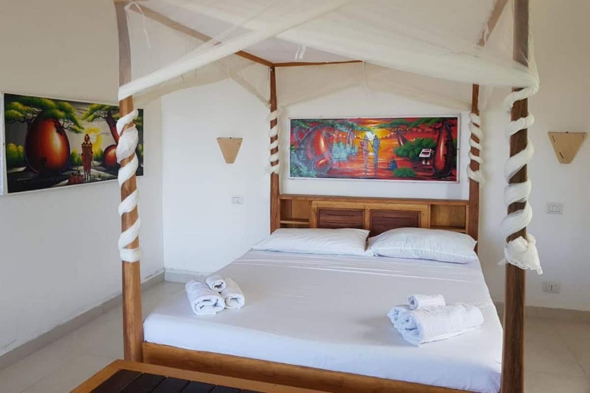 A four-poster bed with a canopy, white linens, and two rolled towels on the bed.