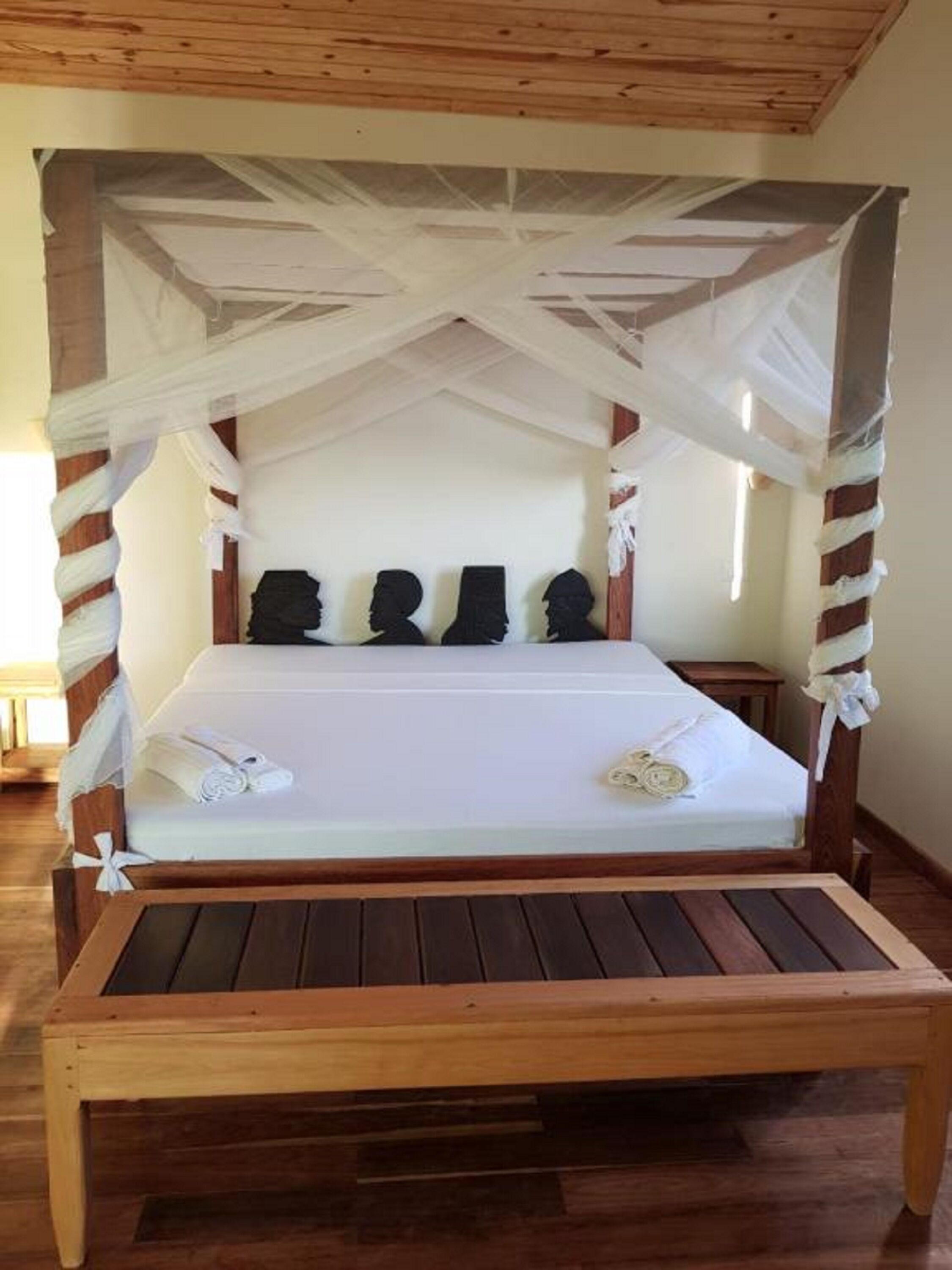 Una cama de madera con dosel, ropa blanca de cama y una mesita de noche.