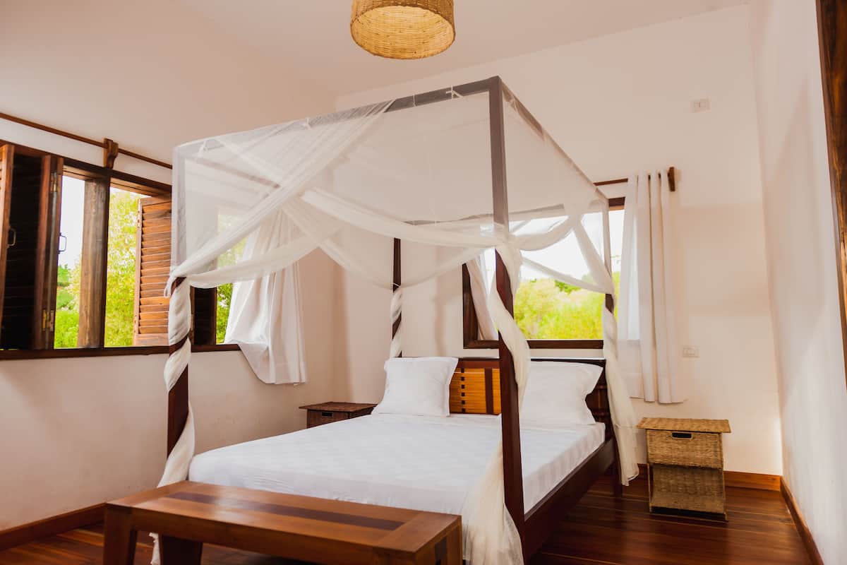 A room with a four-poster bed, wooden flooring, a small wooden table, and a wicker basket.