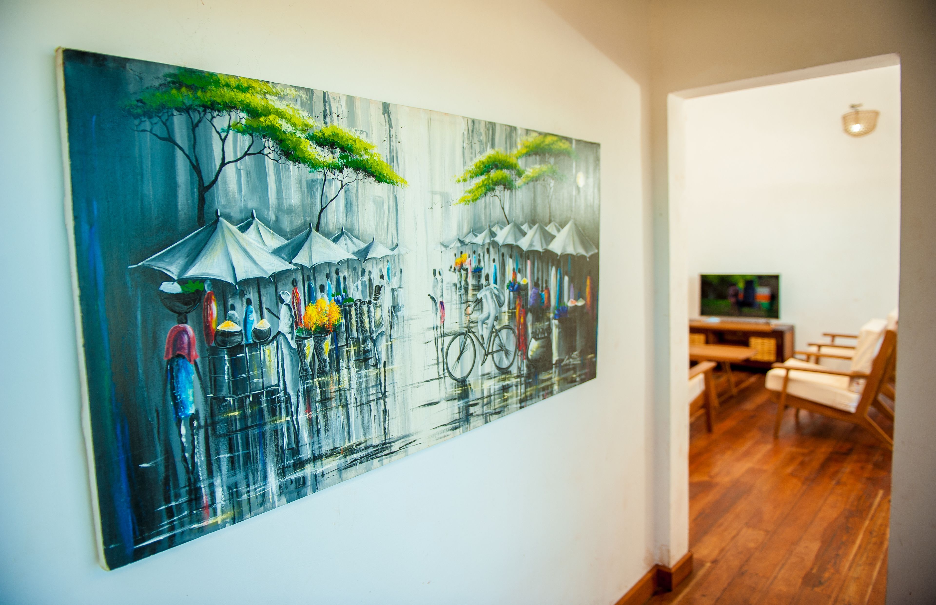 A room with a large painting on the wall depicting a rainy street scene. There is a wooden floor and a television in the corner.