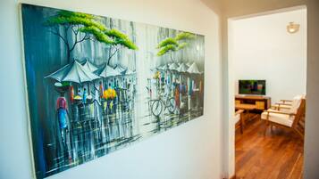 A room with a large painting on the wall depicting a rainy street scene. There is a wooden floor and a television in the corner.