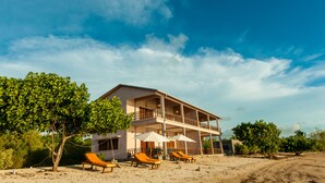A two-story building with a balcony, surrounded by a sandy beach and trees. - Emeraude Lodge (Nosy Be)