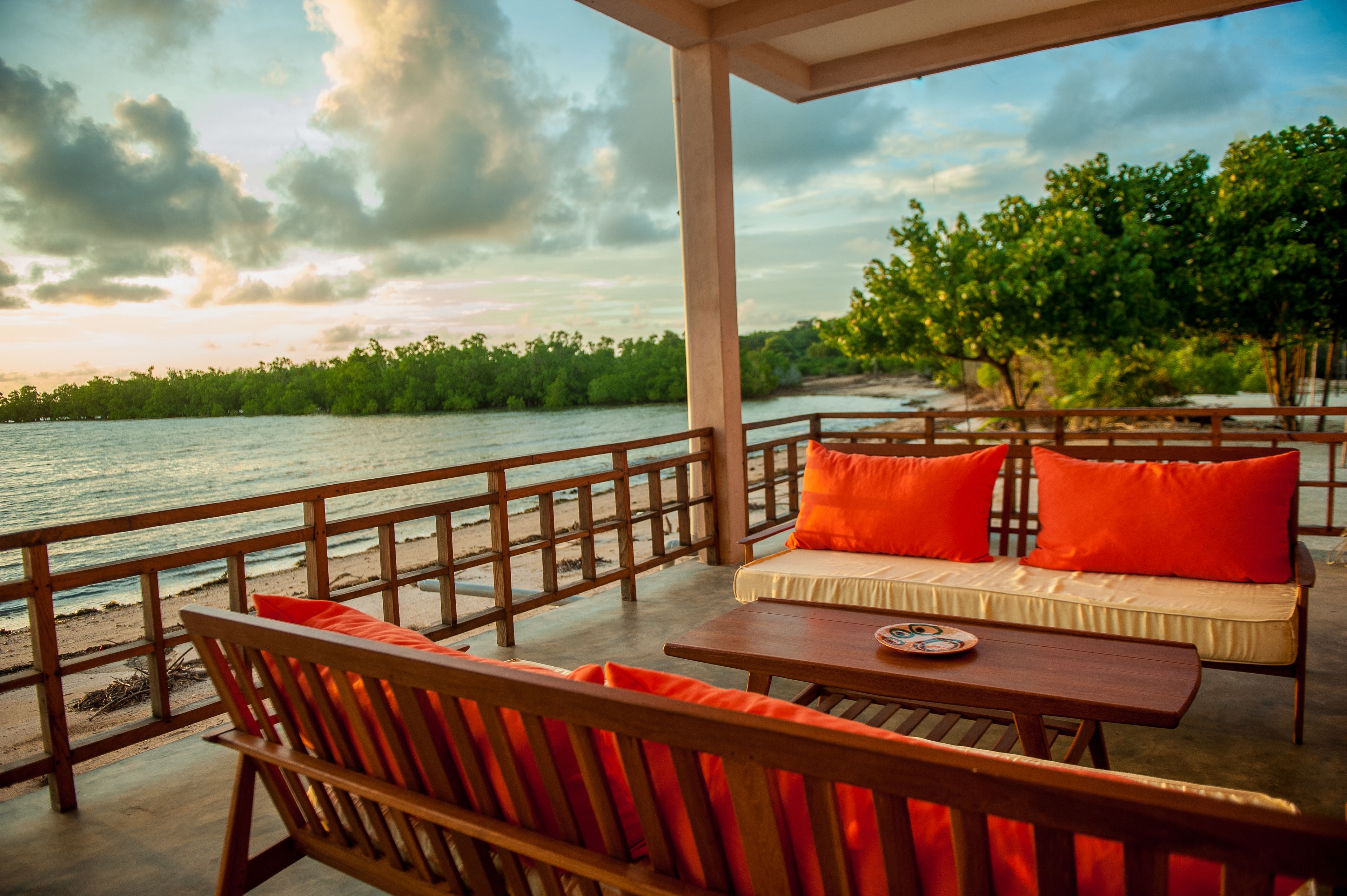 A wooden deck with a sofa and table, overlooking a body of water and greenery.