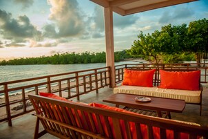 A wooden deck with a sofa and table, overlooking a body of water and greenery.