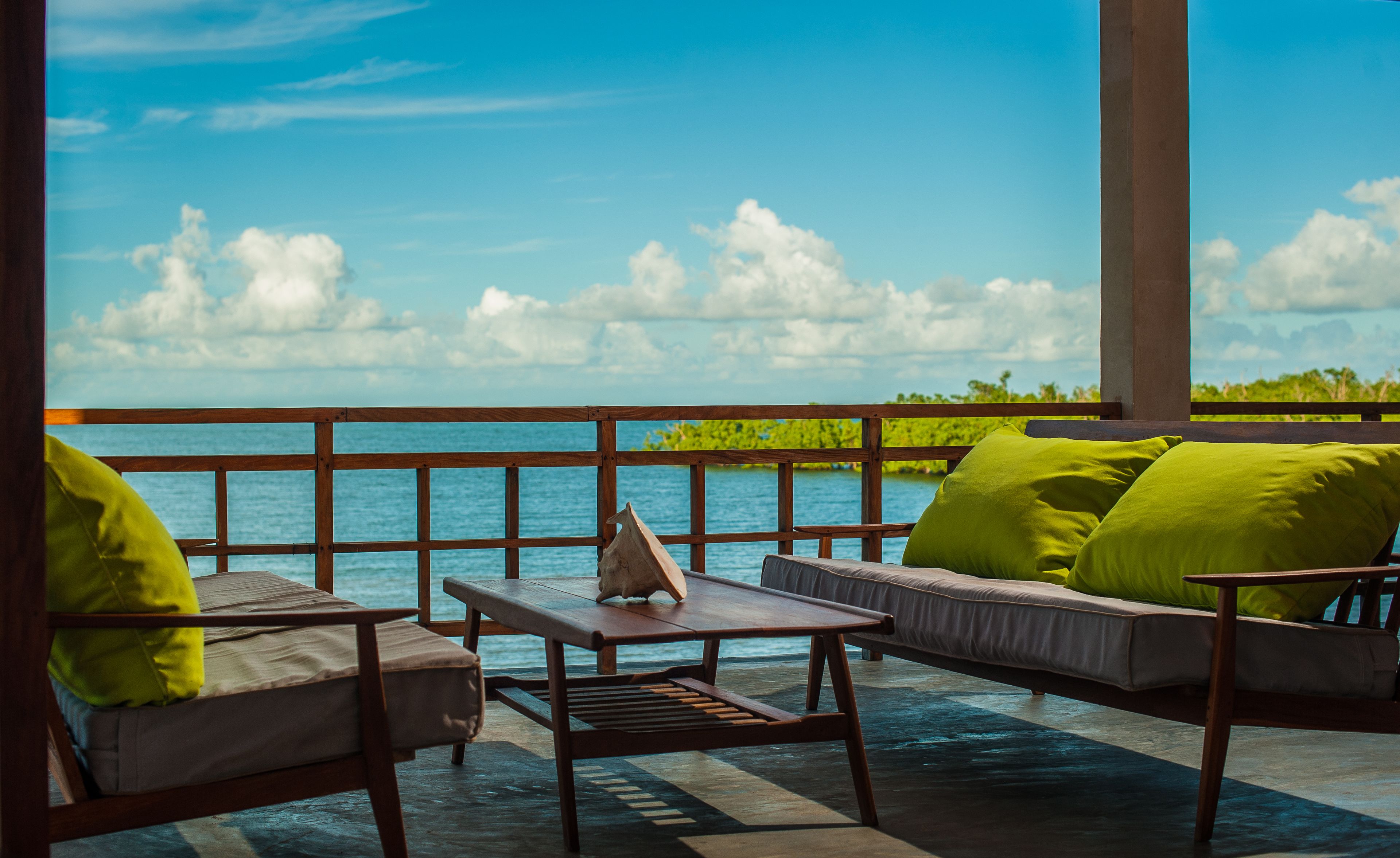 Un balcón con vista al mar, muebles de madera y cojines verdes.