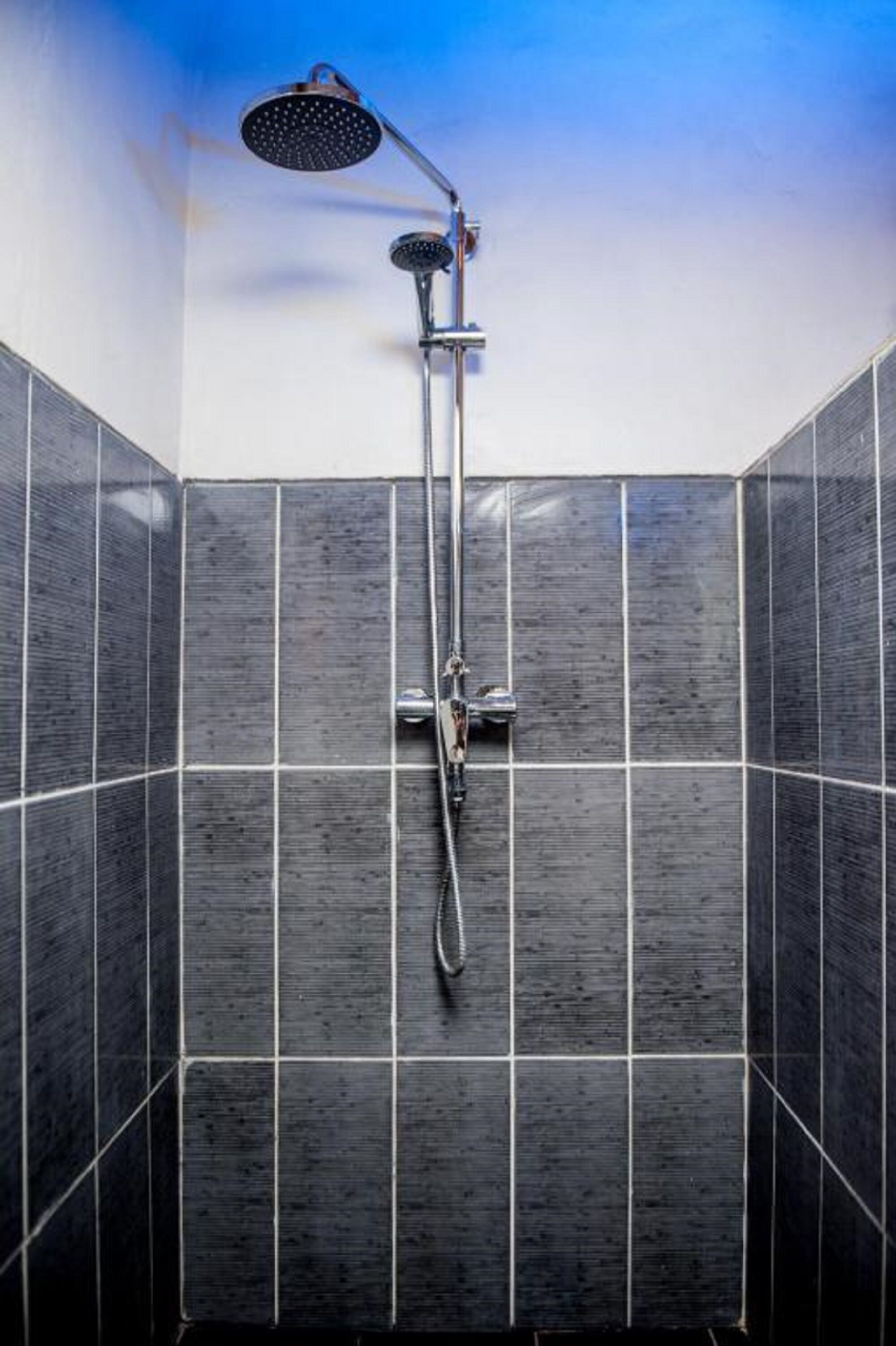 A shower with a handheld showerhead and a wall-mounted faucet in a tiled bathroom.