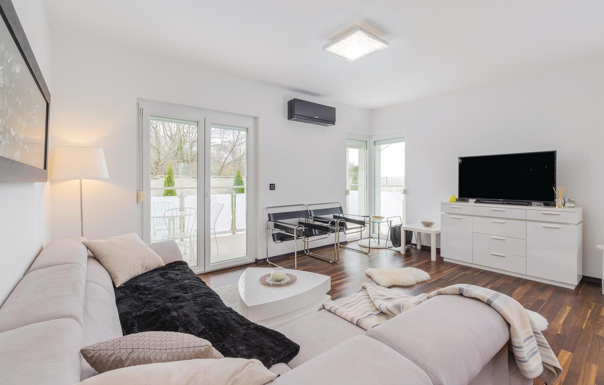 Un salon moderne avec un canapé, une table basse, un téléviseur et un balcon aménagé avec du mobilier d’extérieur.