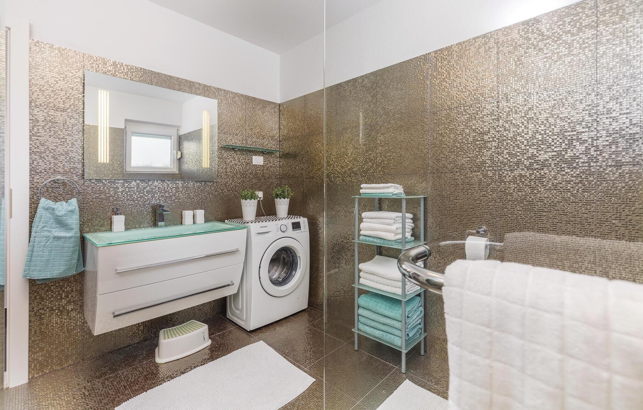 Een moderne badkamer met een wasmachine, een glazen wastafel en een handdoekhouder.
