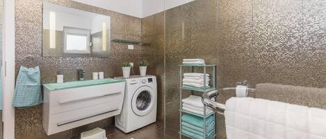 Een moderne badkamer met een wasmachine, een glazen wastafel en een handdoekhouder.