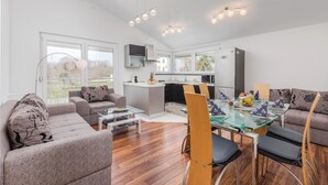 Una sala moderna con una mesa de comedor de vidrio, sofás y una cocina al fondo.