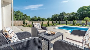 Un patio con mobiliario de mimbre, una piscina y un muro de piedra.