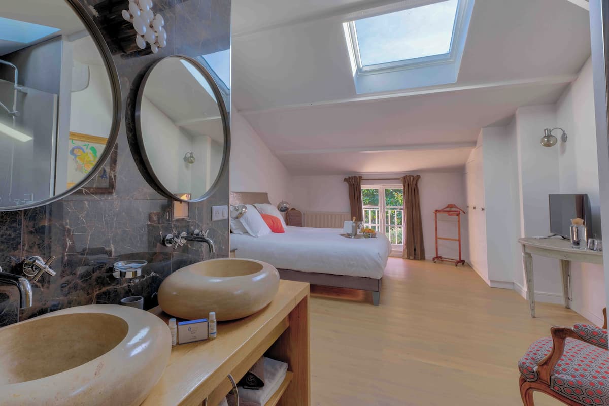 A modern hotel room with a skylight, a large bed, a wooden vanity with two sinks, and a small seating area.