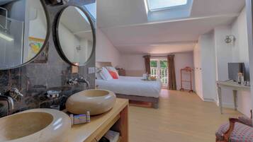 A modern hotel room with a skylight, a large bed, a wooden vanity with two sinks, and a small seating area.