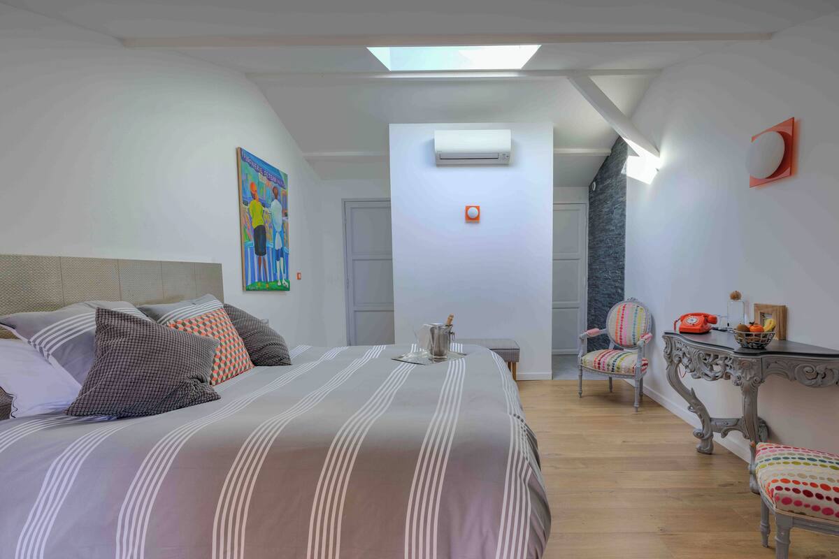 A bedroom with a bed, a chair, a table, and an air conditioning unit.