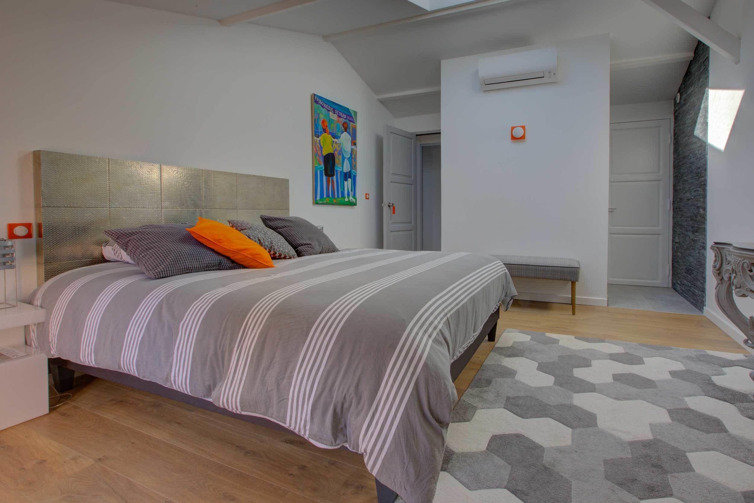 A modern bedroom with a large bed, a headboard, a bench, and a geometric-patterned rug.
