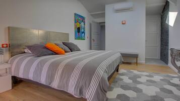 A modern bedroom with a large bed, a headboard, a bench, and a geometric-patterned rug.