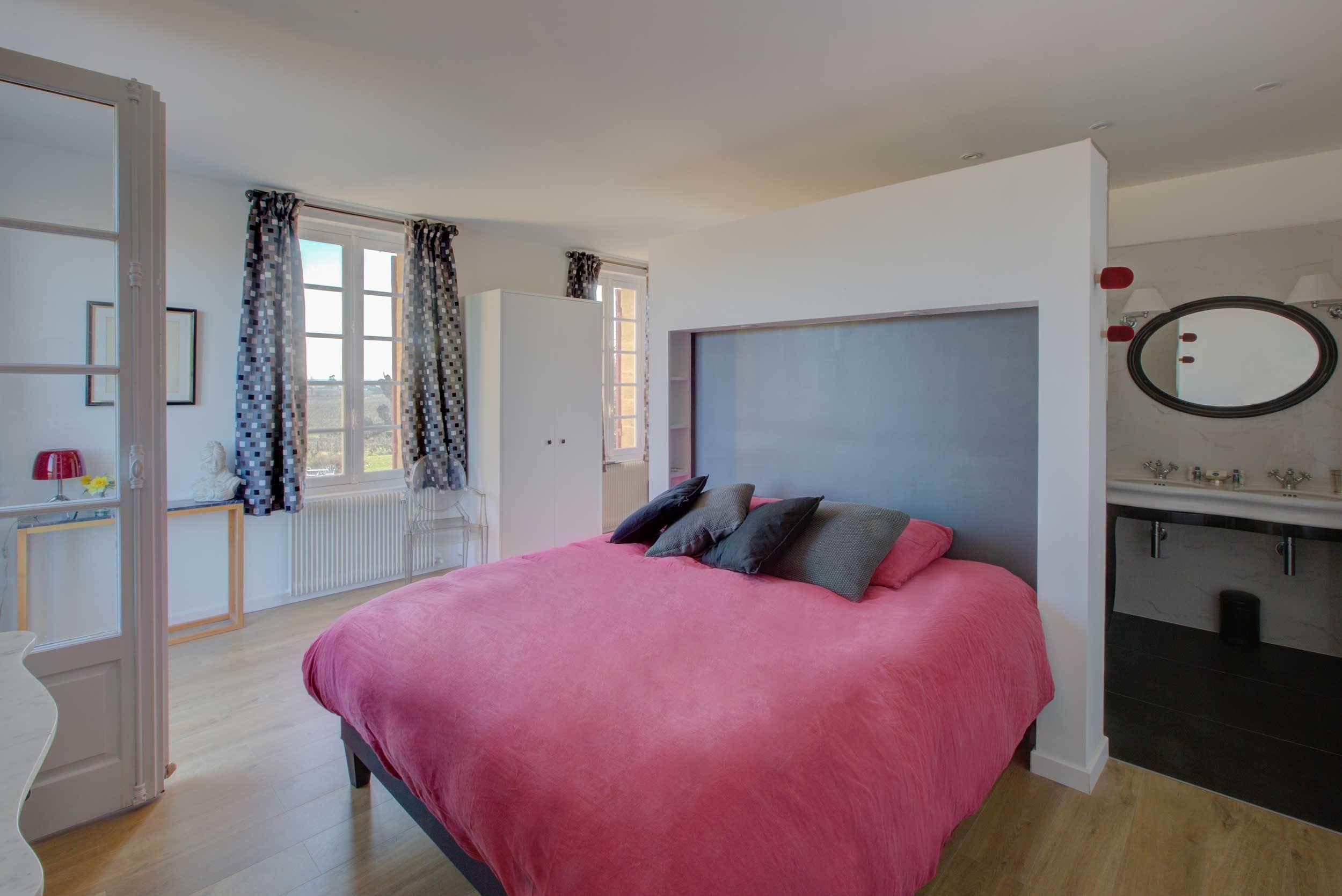 Un dormitorio con una cama grande, un aparador, un espejo y una ventana con cortinas.