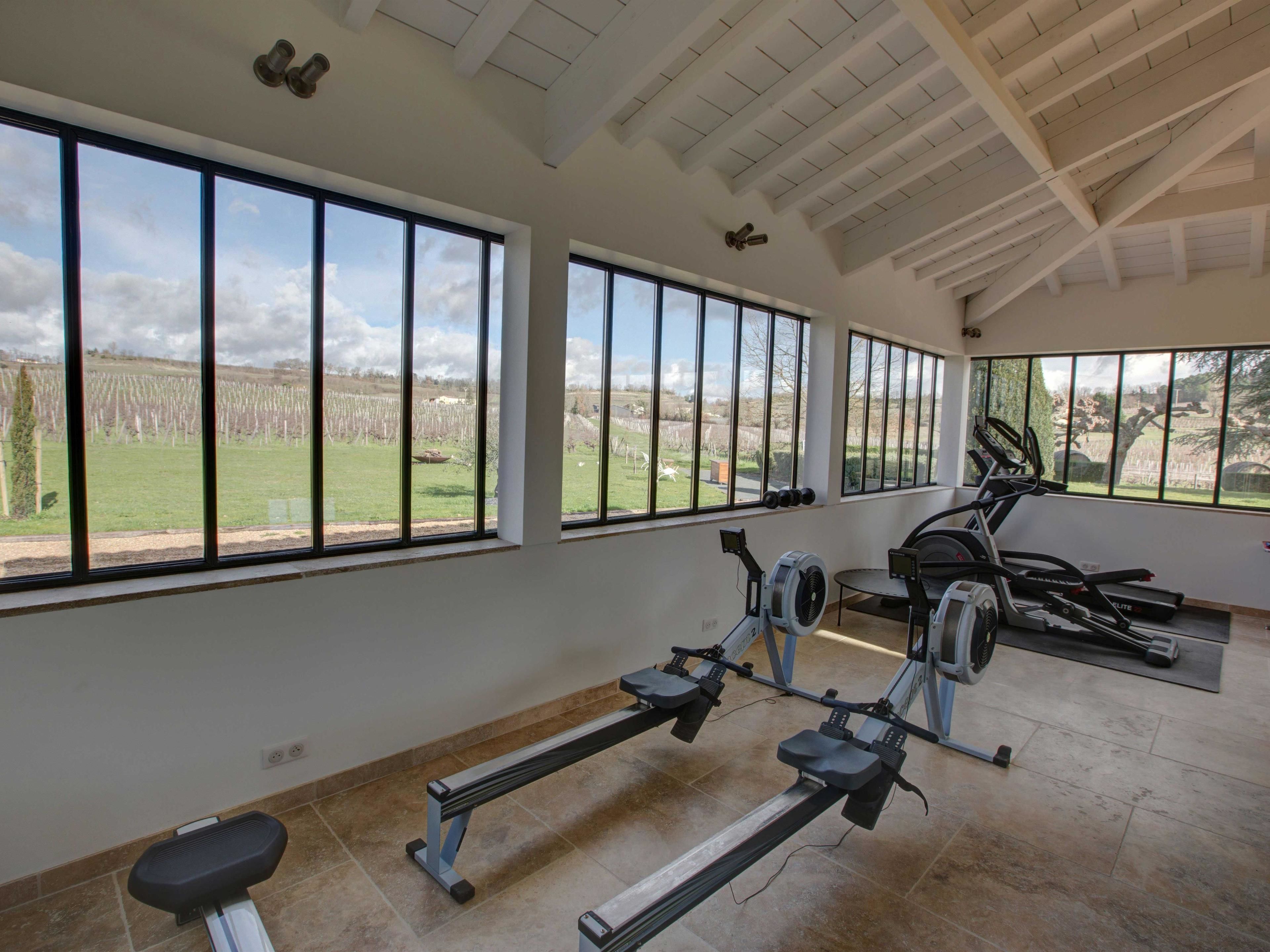 A spacious gym with large windows offering views of a grassy field and trees.