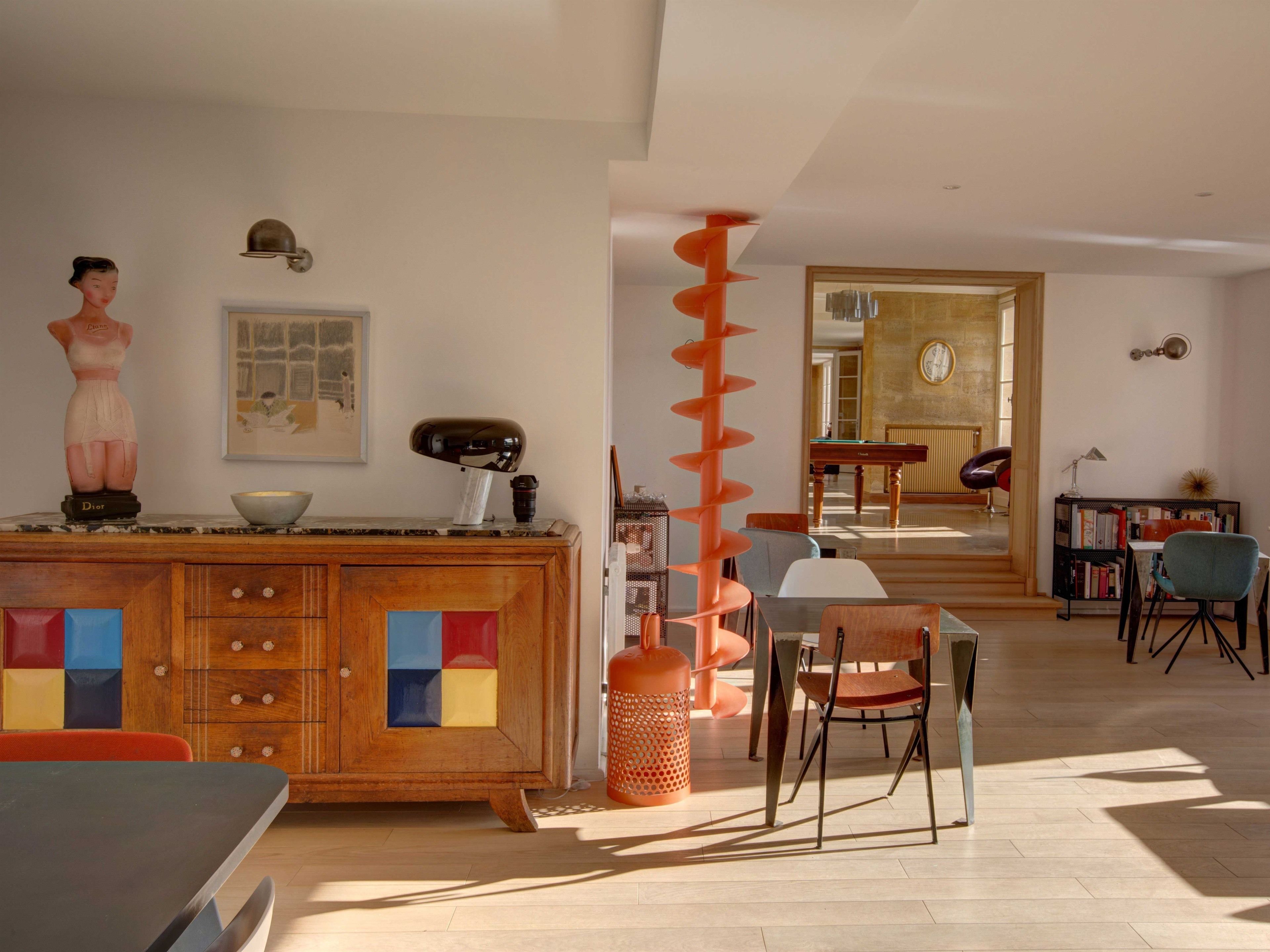 A modern living room with a wooden cabinet, a dining table, and a spiral staircase.