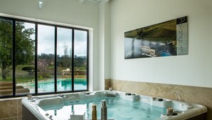 A spa area with a hot tub, a window with a view of a swimming pool and garden, and a framed picture on the wall. - Chateau du Palanquey & SPA (Sainte-Colombe)