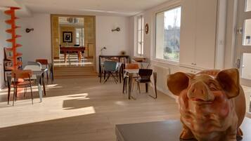 A spacious living room with a large pig sculpture, wooden flooring, and a view of the outdoors through large windows.
