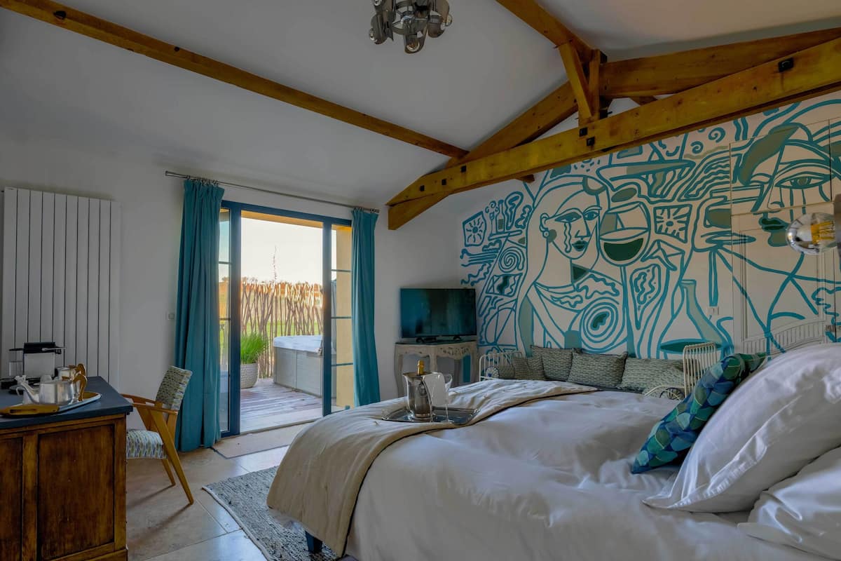 A bedroom with a large bed, wooden beams, a TV, and a mural on the wall.