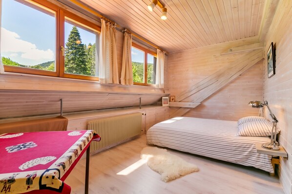 A bedroom with a bed, a table with a red tablecloth, a radiator, and a window with curtains.