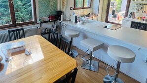 A modern kitchen with a wooden table, bar stools, and a large black pendant light.