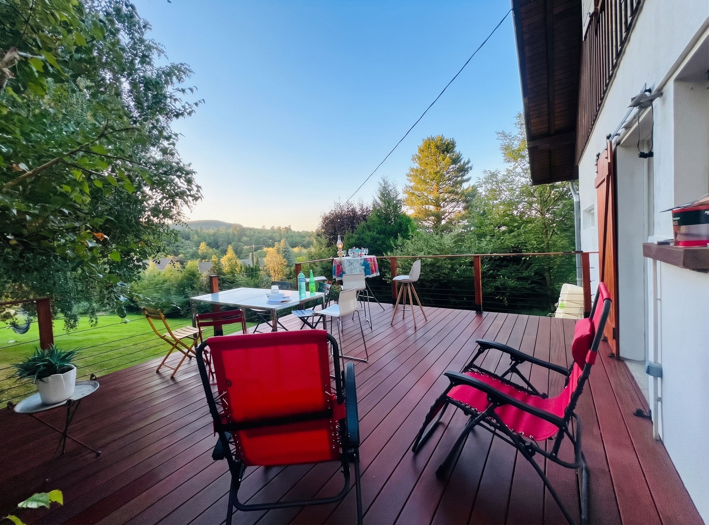 Una terrazza esterna con tavolo e sedie, immersa nel verde e tra gli alberi.