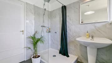 Een moderne badkamer met een douche, wastafel en een potplant.