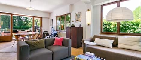 A modern living room with a sofa, a coffee table with books, and a dining area with a table and chairs.