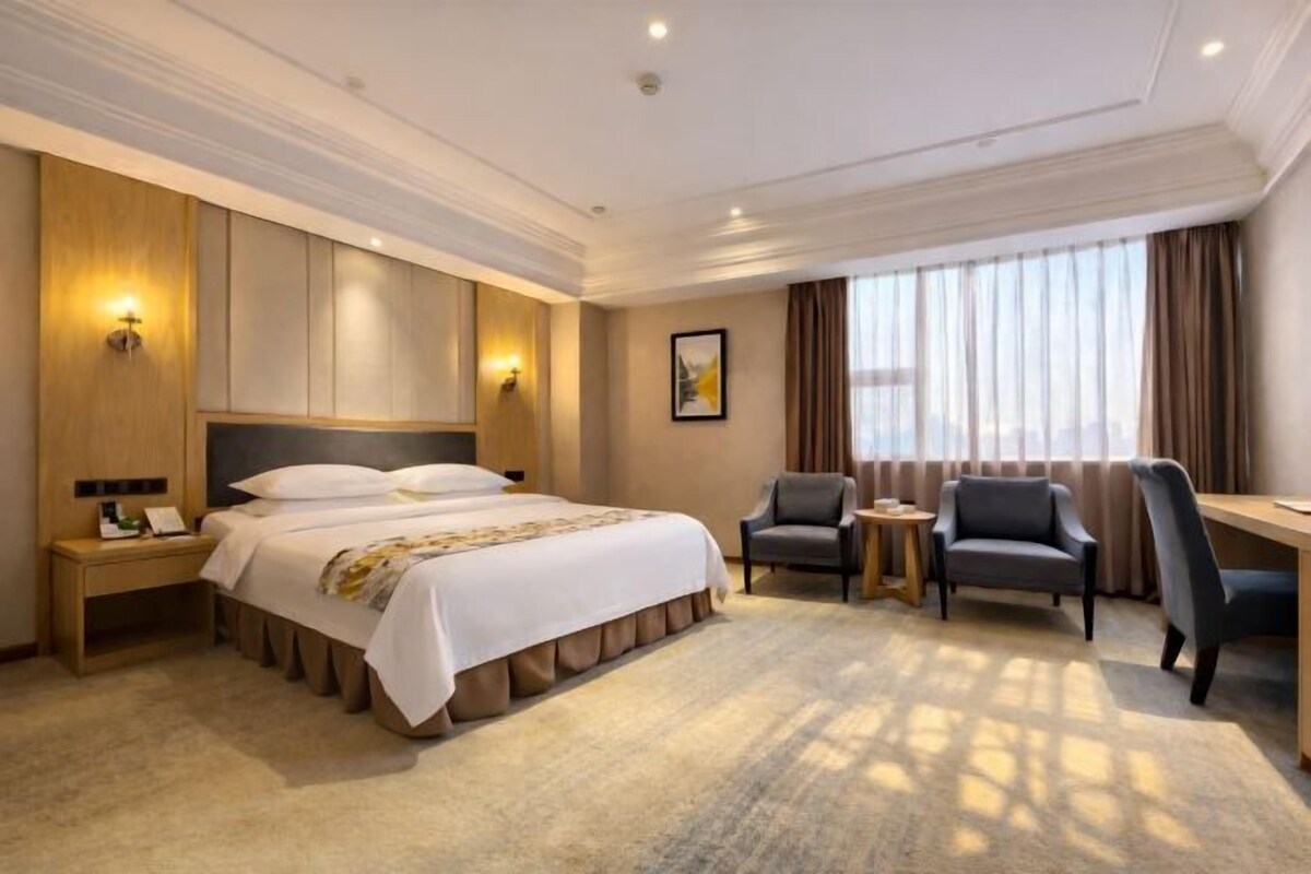 A hotel room with a large bed, two armchairs, a desk, and a nightstand.