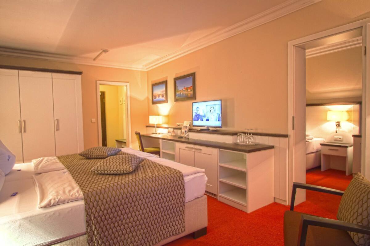 Ein Hotelzimmer mit Bett, Schreibtisch, Fernseher und einer kleinen Küchenzeile.