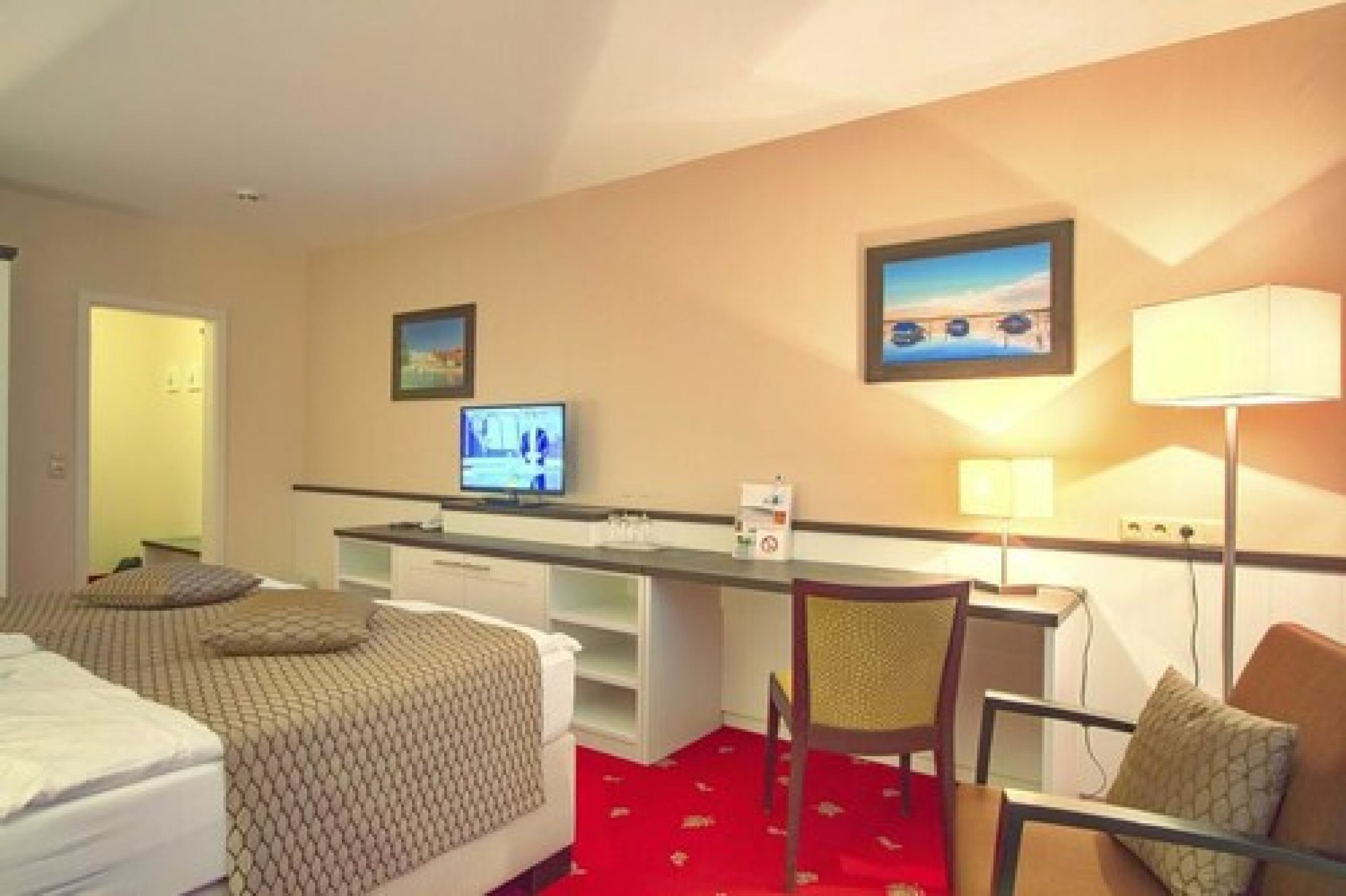 Habitación de hotel con dos camas, un escritorio con computadora, una silla y un televisor.