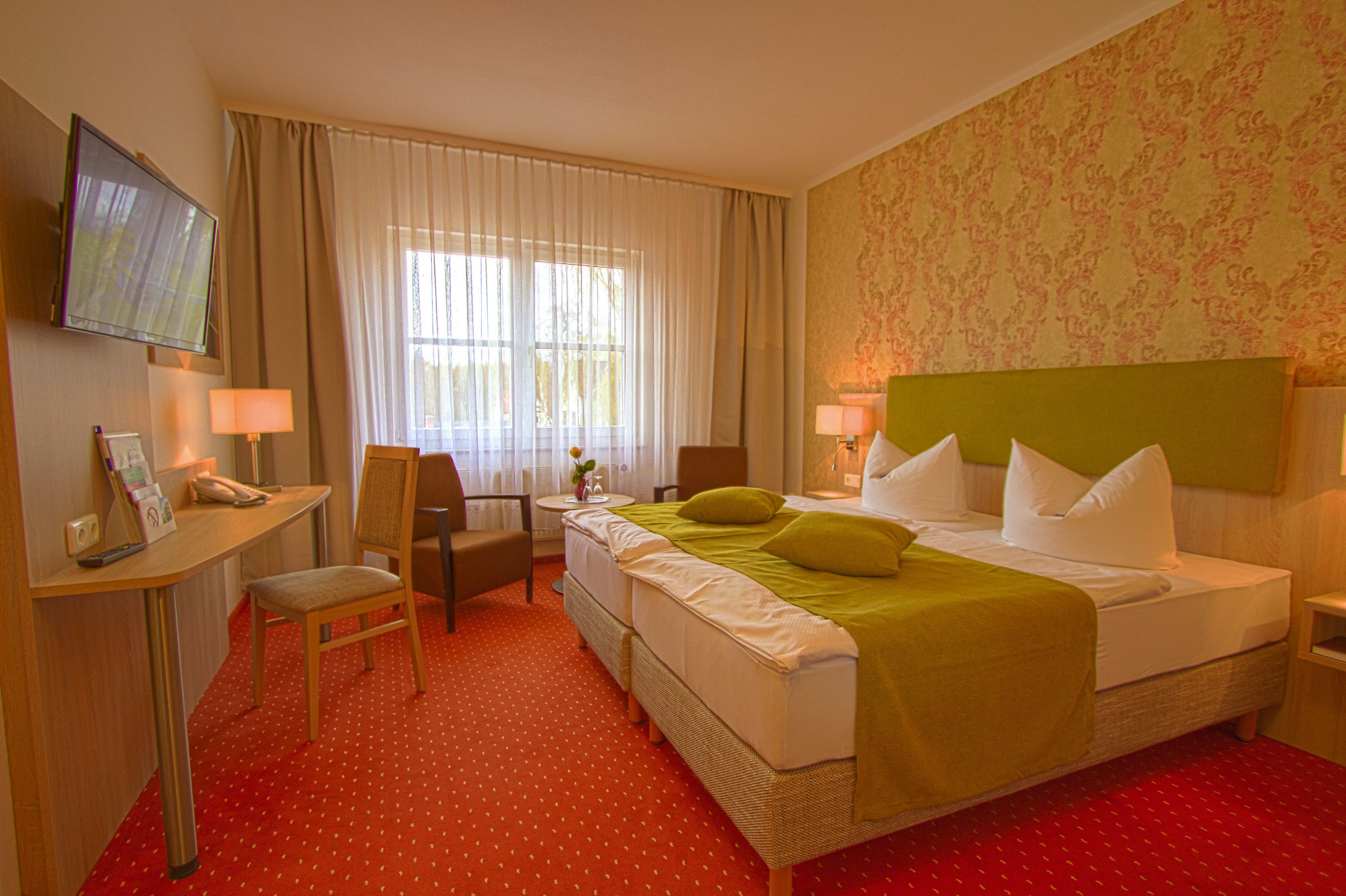 A hotel room with a bed, a desk, a chair, a TV, and a window with curtains.