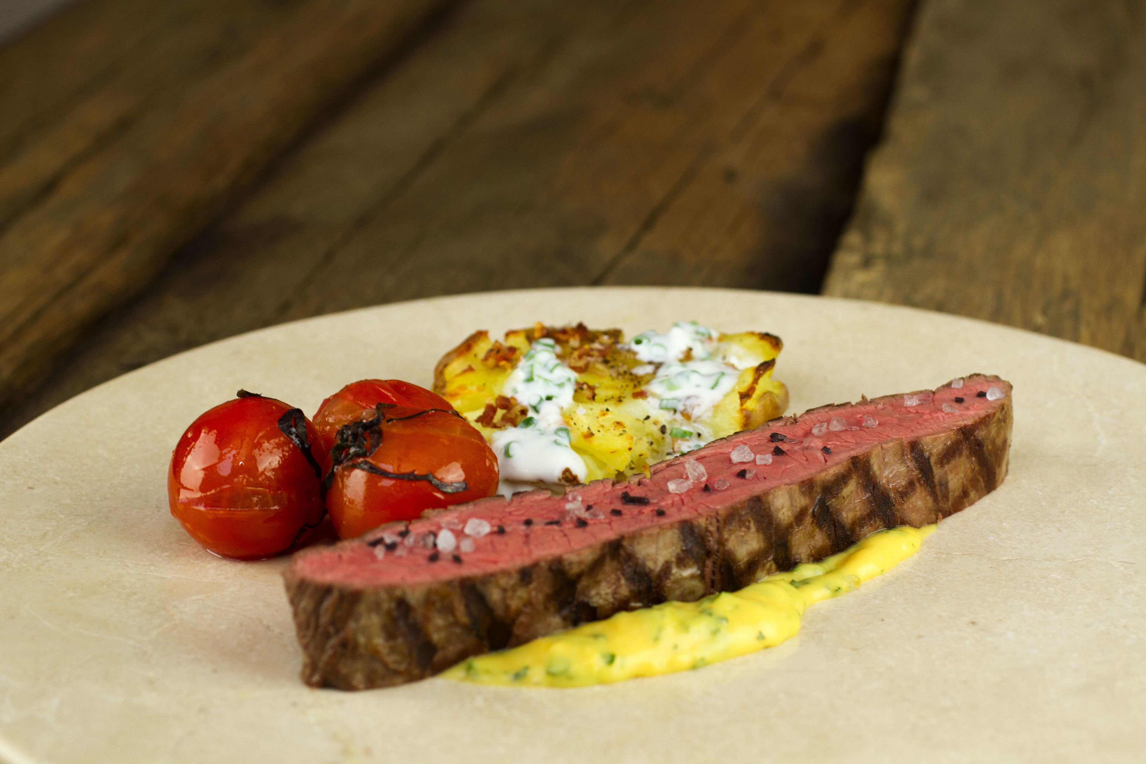 Un plato con bistec, tomates y un guiso de patatas.