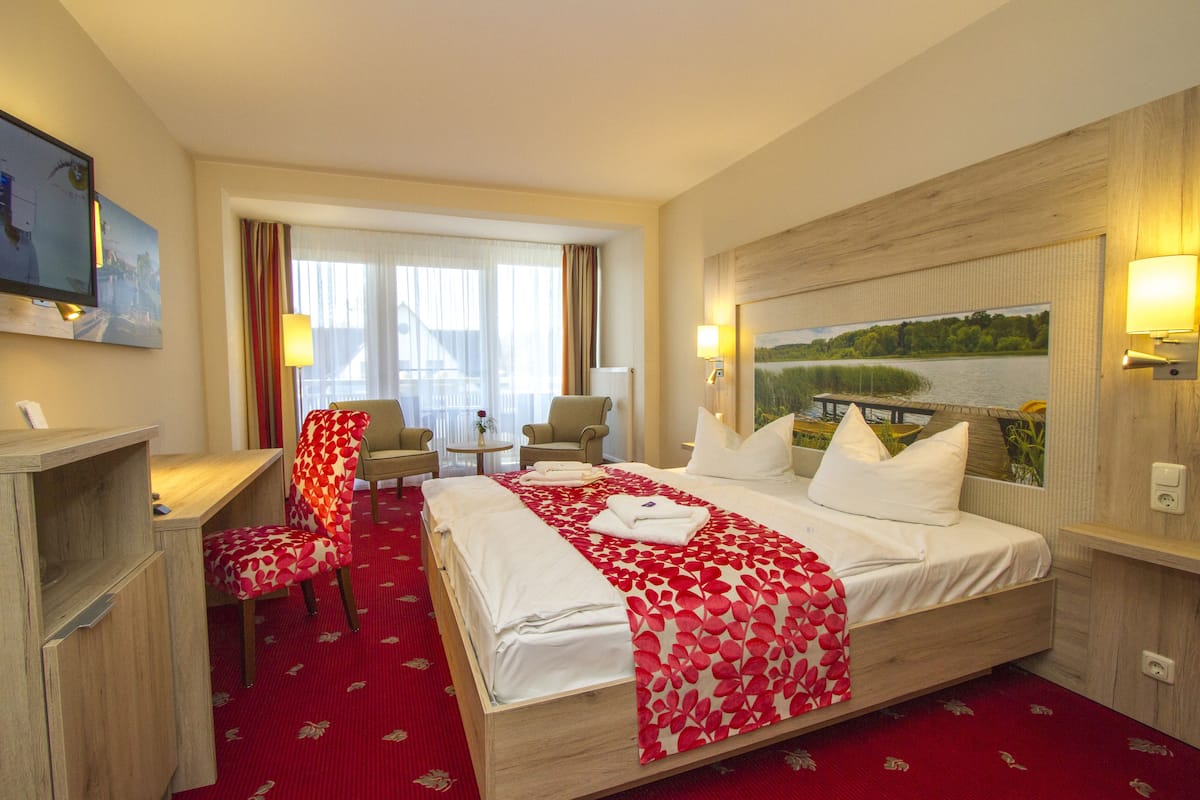 Ein Hotelzimmer mit einem großen Bett, einem Schreibtisch, zwei Stühlen, einem Fernseher und einem Bild an der Wand.