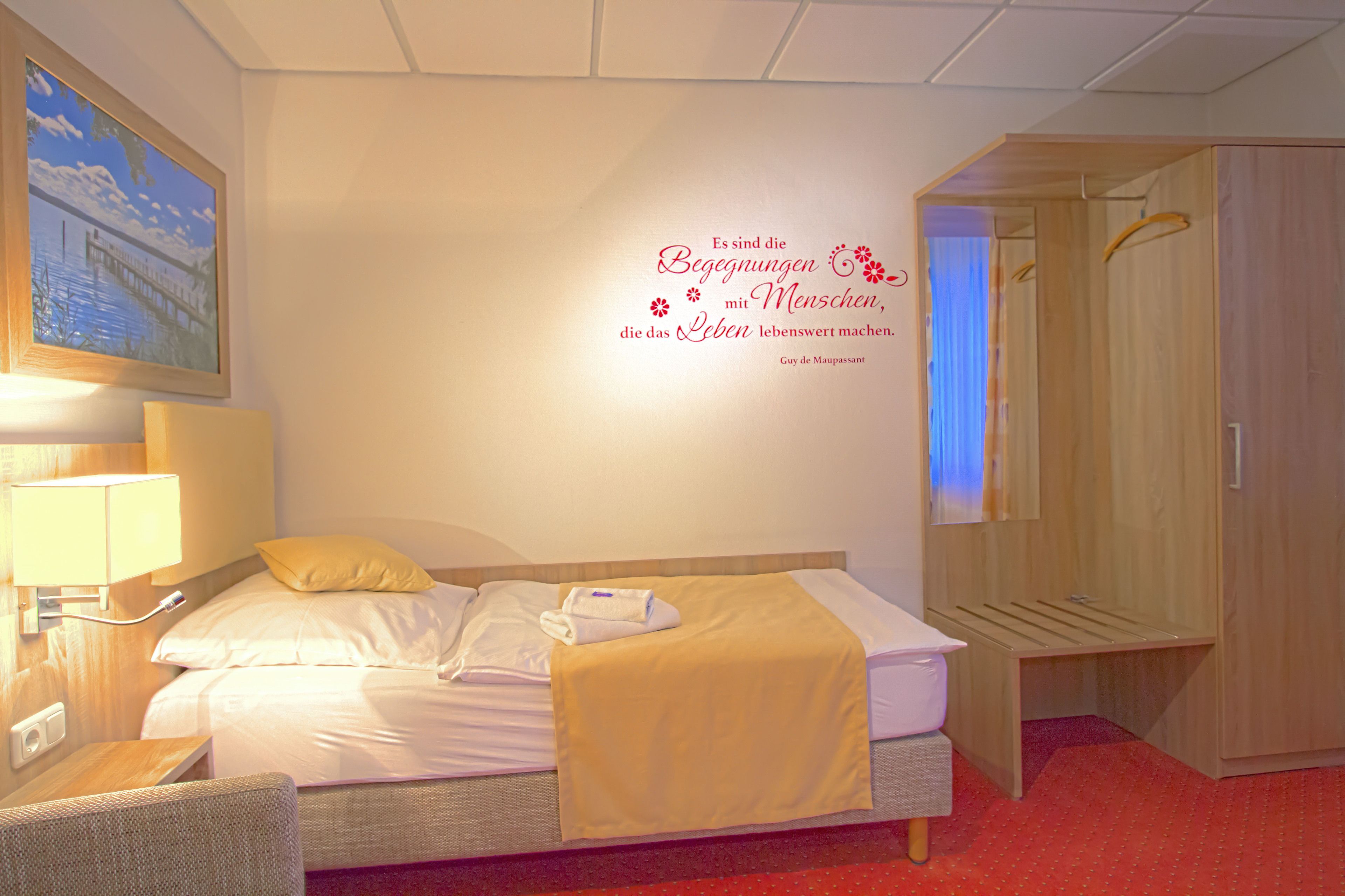 Una habitación de hotel con cama, mesita de noche, lámpara, decoración en la pared y armario.