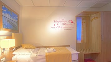 Ein Hotelzimmer mit Bett, Nachttisch, Lampe, Wandbild und Kleiderschrank.