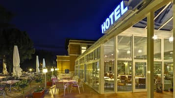 A hotel with an outdoor patio area featuring tables and chairs, a glass entrance, and a prominent 'HOTEL' sign.
