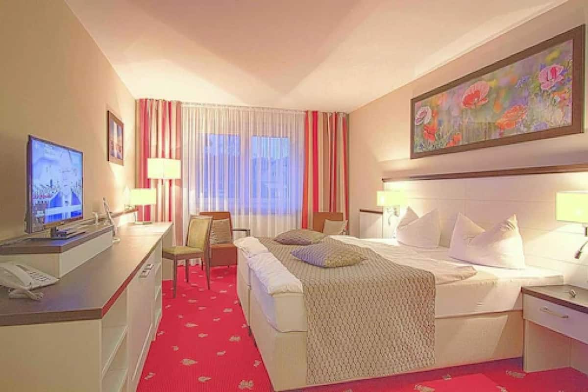 Ein Hotelzimmer mit einem Bett, Nachttischen, einem Schreibtisch mit Computer, einem Sessel und einem Fernseher.